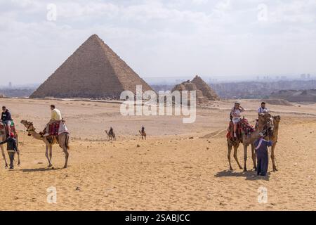 Turisti che cavalcano cammelli di fronte alle piramidi di Giza, Egitto Foto Stock