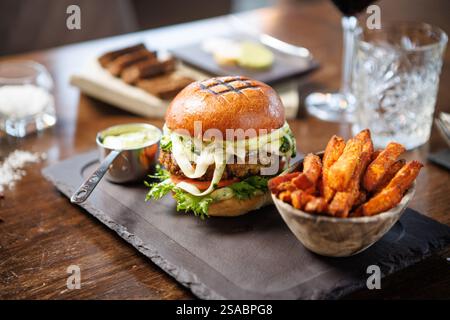 Hamburger vegetariano con verdure fresche, pomodoro, formaggio e salsa cremosa su panino alla brioche. Accompagnato da una ciotola di patatine dolci e una tazza di metallo di Foto Stock