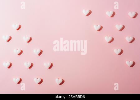 Piccoli cuori di caramelle bianche disposti su uno sfondo rosa pastello con ombre. Il giorno di San Valentino. Trama, sfondo con spazio di copia. Foto Stock