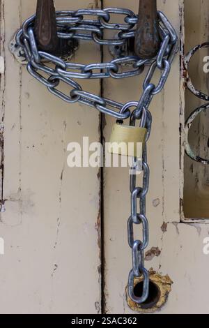 Il fascino rustico incontra la sicurezza in questa immagine ravvicinata che mostra un lucchetto a catena su una porta vecchia. Foto Stock