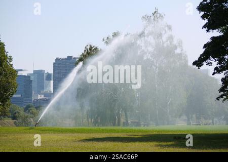 Sistema di irrigazione sull'isola del Danubio Donauinsel a Vienna. Innaffiare prati e alberi nel parco in una calda giornata estiva. Agricoltura per la protezione della siccità Foto Stock
