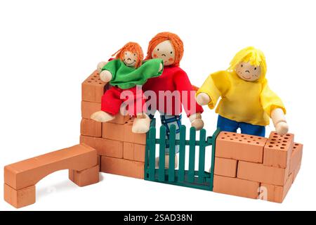 Natura morta con una piccola famiglia di bambine che costruisce una casa con un bambino seduto su mattoni su sfondo bianco. Foto Stock