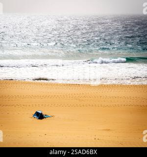 Una tenda blu solitaria su una spiaggia sabbiosa con dolci onde che lambiscono sulla riva. La scena è tranquilla, con impronte nella sabbia che conducono verso la W Foto Stock