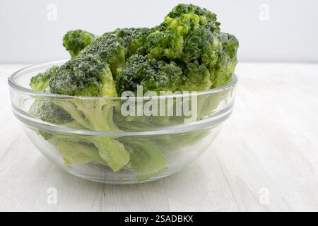 Broccoli congelati in un recipiente su una scrivania di legno bianca. Conservare e cucinare verdure in casa Foto Stock