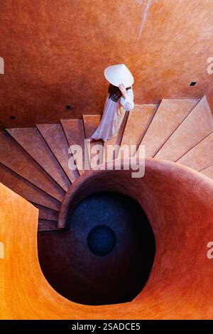 Bella donna che indossa un abito bianco e un cappello conico che cammina lungo la scala a chiocciola Foto Stock