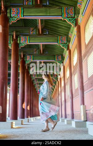 Una donna turistica in un abbigliamento colorato esplora gli interni vibranti e decorati in modo complesso di un tradizionale tempio coreano a Seoul, Corea del Sud. Foto Stock