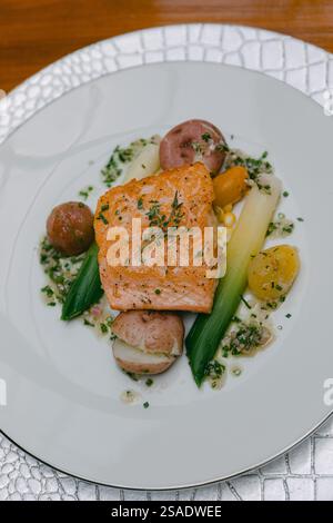 Un filetto di salmone perfettamente grigliato si trova su un letto di colorate verdure di stagione, guarnite con erbe fresche. Il piatto è presentato su un piatto elegante Foto Stock