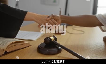 Donna che stringe la mano in tribunale con il martelletto del giudice sulla scrivania, sottolineando la fiducia e l'accordo all'interno Foto Stock