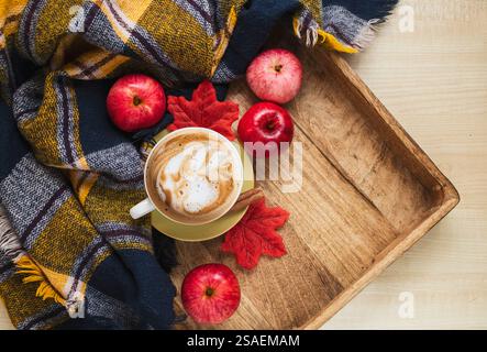 Accogliente composizione autunnale con plaid caldo, tazza di caffè e mele rosse su vassoio in legno Stagione autunnale. Foto Stock