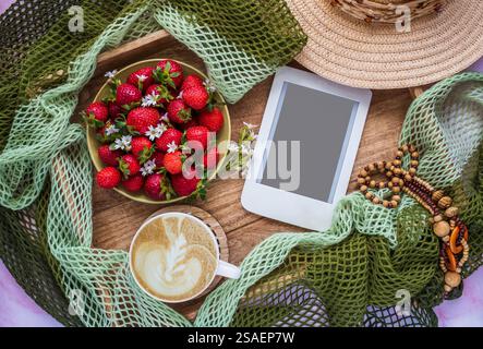 Composizione romantica con tazza di caffè, piatto di fragole succose ed e-Reader con spazio per le copie su vassoio di legno Modello per blog femminile. Foto Stock