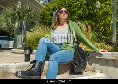 Giovane donna d'affari che gode di un momento di pace all'aperto, sorseggiando un caffè dopo una giornata di lavoro produttiva Foto Stock