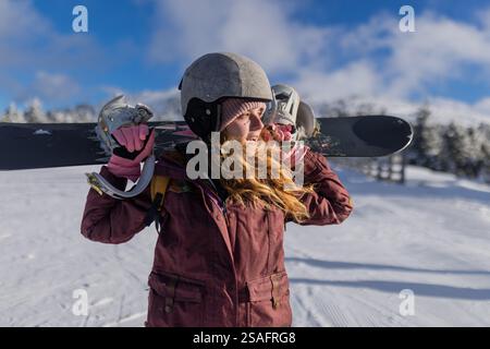 Uno snowboarder che indossa l'equipaggiamento e porta il suo snowboard si erge su un paesaggio di montagna innevato, godendo di sport invernali all'aperto e di una neve panoramica Foto Stock