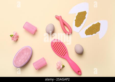 Accessori per parrucchieri con fiori, uovo di Pasqua e orecchie da coniglio su sfondo beige Foto Stock