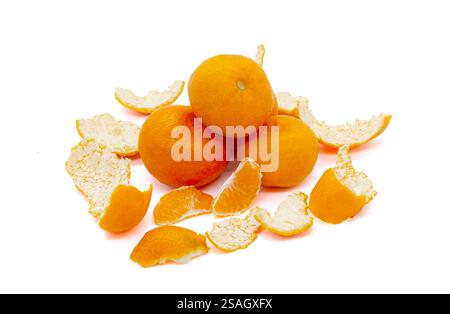 Tre mandarini interi, circondati da pezzi della loro buccia, adagiati su uno sfondo bianco. Arancio brillante mandarini freschi e succosi su un backgroun bianco Foto Stock
