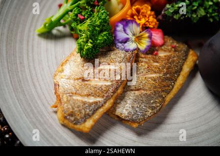 Filetto di pesce scottato in padella con verdure vivaci, tra cui broccoli, pomodori ciliegini e costolette di carote, guarnite con fiori commestibili. Accompagnato da Foto Stock