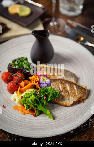 Filetto di pesce scottato in padella con verdure vivaci, tra cui broccoli, pomodori ciliegini e costolette di carote, guarnite con fiori commestibili. Accompagnato da Foto Stock