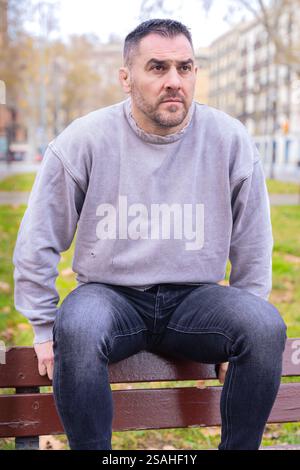 Uomo premuroso seduto su una panchina da parco in casual outfit. Verticale Foto Stock