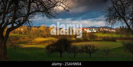 Piccolo villaggio su una collina panoramica in un paesaggio rurale panoramico con una luce suggestiva, con sagome di alberi e case illuminate Foto Stock