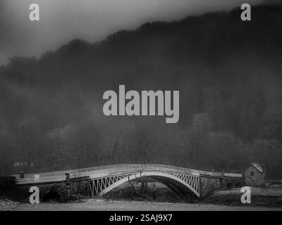 Un ponte in metallo ornato sopra un fiume in Una valle con Una collina nebbiosa Foto Stock