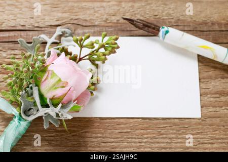 Fiore all'occhiello con rosa rosa rosa, penna e carta bianca su un tavolo di legno marrone. Foto Stock