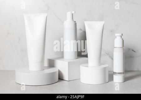 Bellissimi modelli cosmetici per annunci pubblicitari, tubi in plastica e bottiglie su sfondo bianco con podi. Design estetico per prodotti di qualità superiore Foto Stock