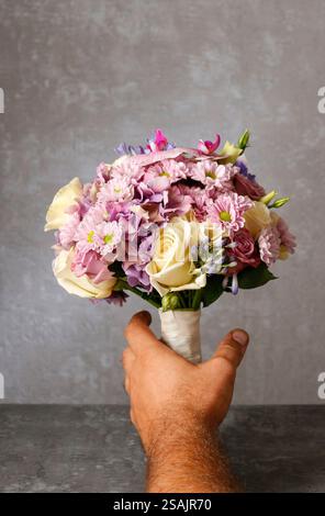 Uomo che prende un bouquet, copia spazio. Delizioso bouquet di orchidee rosa, crisantemi e ortensie mescolate con rose gialle e ustomi viola. Foto Stock