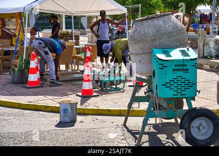Sint Maarten, Caraibi - 3 gennaio 2025: Operai edili in un sito sull'isola caraibica di Sint Maarten lavorano alla riparazione del marciapiede con un miscelatore di calcestruzzo e barriere di sicurezza *** Bauarbeiter auf einer Baustelle auf der Karibikinsel Sint Maarbeiten un einer Gehwegreparatur mit einer Betonmischmaschine und Sicherheitsabsperrungen Foto Stock