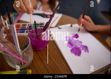 Attività artistica creativa che coinvolge la pittura ad acquerello su carta, illustrando la creatività di un bambino e l'attenzione all'arte. Colori vivaci, pennelli e a. Foto Stock