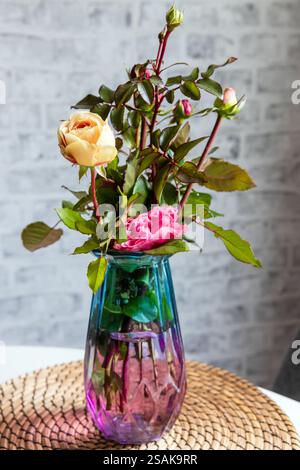 Un bouquet di rose colorate si staglia in un vaso di vetro sullo sfondo di una parete di mattoni grigi, foto verticale Foto Stock