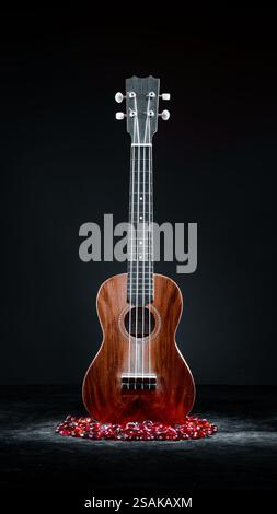 Ukulele, pittura chiara su sfondo scuro, marrone, primo piano nero e perle di vetro rosso. 2025 Foto Stock
