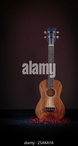 Ukulele, pittura chiara su sfondo scuro, marrone, primo piano nero e perle di vetro rosso. 2025 Foto Stock