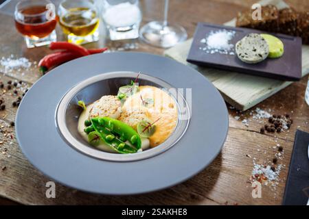 Capesante con schiuma di gamberi, crema di cavolfiore e piselli verdi su un piatto. Delizioso e salutare primo piano di pesce servito per pranzo su un tavolo in stile moderno Foto Stock