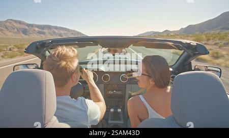 Vista posteriore della coppia giovane durante il viaggio in auto con capote lungo la strada di campagna Foto Stock