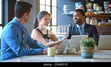 Tre uomini d'affari seduti al tavolo che lavorano al computer portatile nel bar Foto Stock