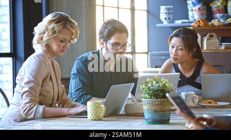 Tre uomini d'affari seduti al tavolo che lavorano al computer portatile nel bar Foto Stock
