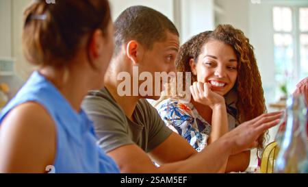 Primo piano di un gruppo di giovani amici seduti intorno al tavolo a casa gustando un pasto insieme Foto Stock