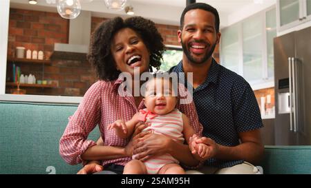 Ritratto di una famiglia sorridente seduta sul divano a casa che tiene in mano una bambina Foto Stock