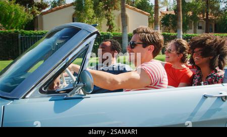 Vista laterale del gruppo di giovani amici durante il viaggio in auto con capote d'epoca Foto Stock