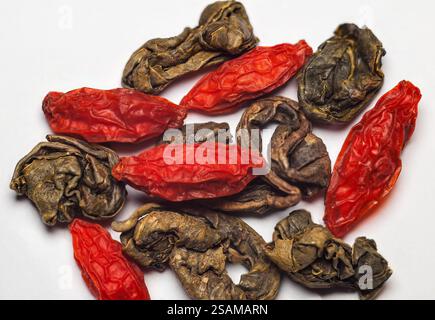 Primo piano di bacche di goji secche miste e foglie di tè verde arrotolate per la preparazione del tè. Foto Stock