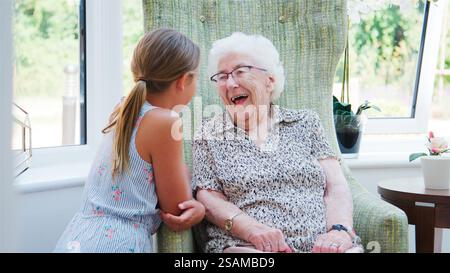 Nipote seduta a parlare con la nonna ridendo durante la visita alla casa di riposo Foto Stock