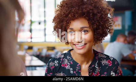 Primo piano di una giovane donna che incontra gli amici seduti al Table Inside Coffee Shop e parla Foto Stock