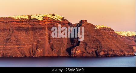 Una splendida vista di una scogliera rocciosa con texture a strati, che si affaccia su un mare calmo. La calda luce dorata del tramonto proietta un bel bagliore sulla terra Foto Stock