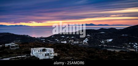 Uno splendido tramonto su un paesaggio costiero caratterizzato da colline ed edifici bianchi sparsi. Il cielo è pieno di colori vivaci, che si riflettono sulla cal Foto Stock