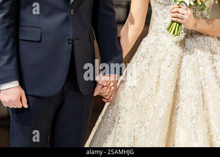 Un uomo e una donna si stanno tenendo per mano. Quell'uomo indossa un vestito e una cravatta. La donna sta indossando un abito da sposa Foto Stock