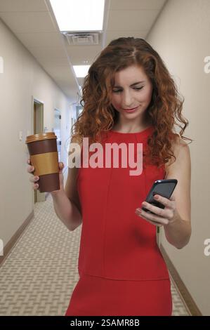 Donna che utilizza un telefono cellulare e tenendo un dispositivo monouso per andare tazza da caffè Foto Stock