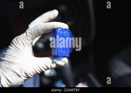 Mano con i guanti che regge un adattatore blu all'interno di un'auto Foto Stock