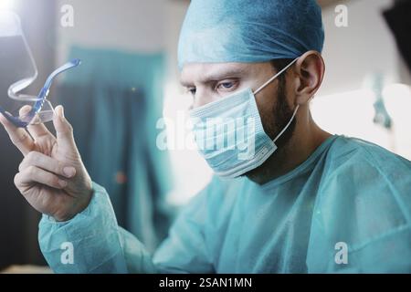 Il chirurgo in scrub blu tiene con cura i suoi occhiali Foto Stock