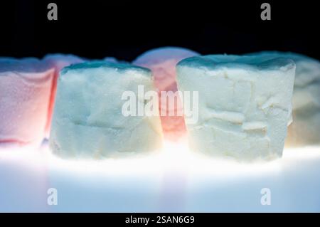 Vista ravvicinata di diversi marshmallow piccoli, strutturati, di colore chiaro e color pastello. I marshmallow appaiono su uno sfondo Foto Stock