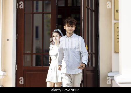 Una coppia esce da un edificio, tenendosi per mano in un abbigliamento formale Foto Stock