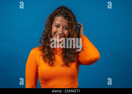 Donna sicura di sé con top arancione che posa su sfondo blu Foto Stock